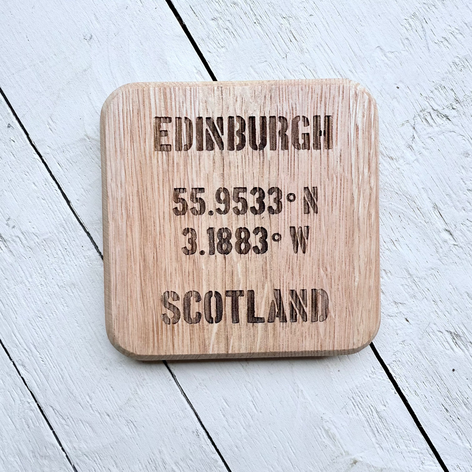 Barrel Oak Wooden coaster with engraved Edinburgh and coordinates on a light wooden surface