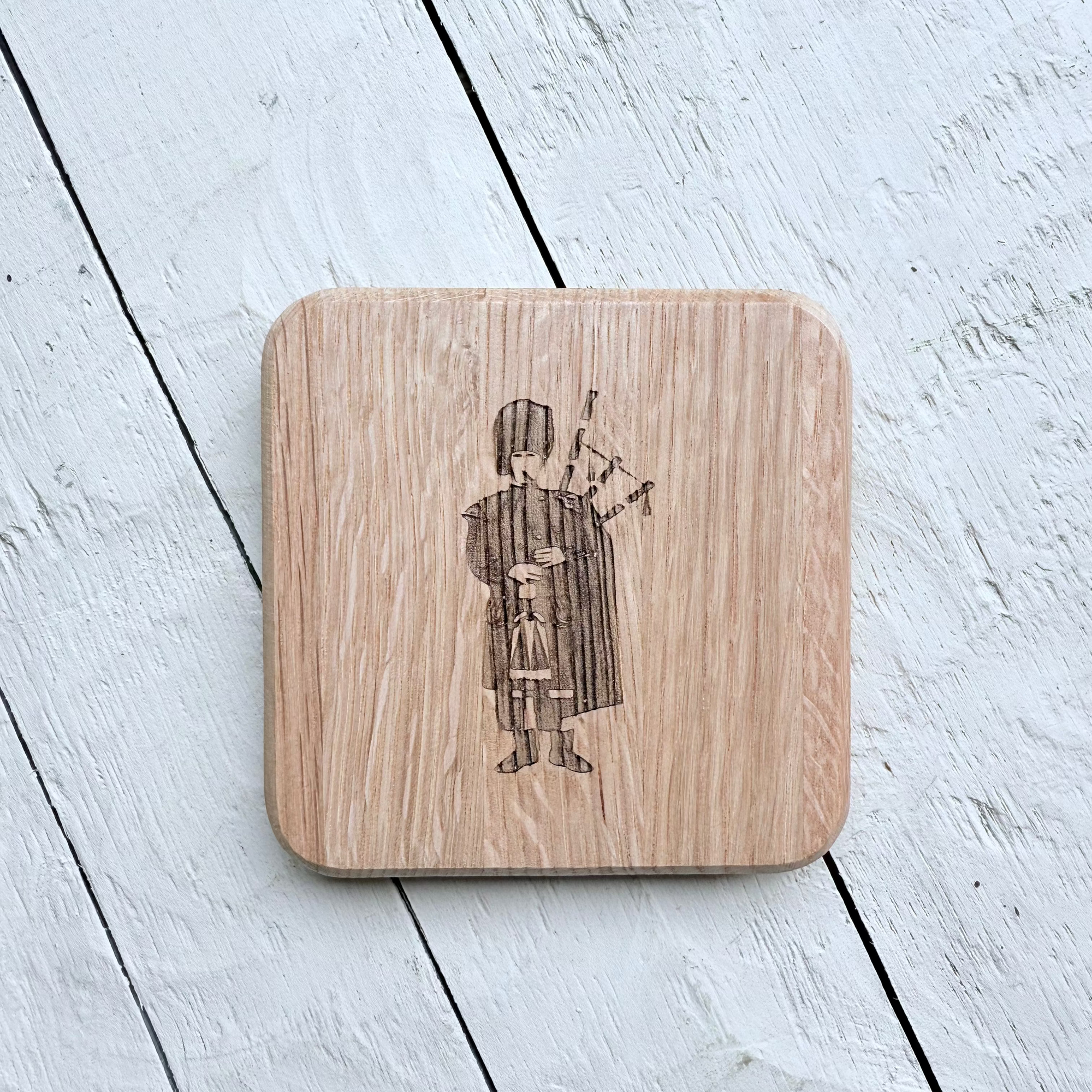 Barrel Oak Wooden coaster with an engraved design of a person playing bagpipes on a light wooden surface.