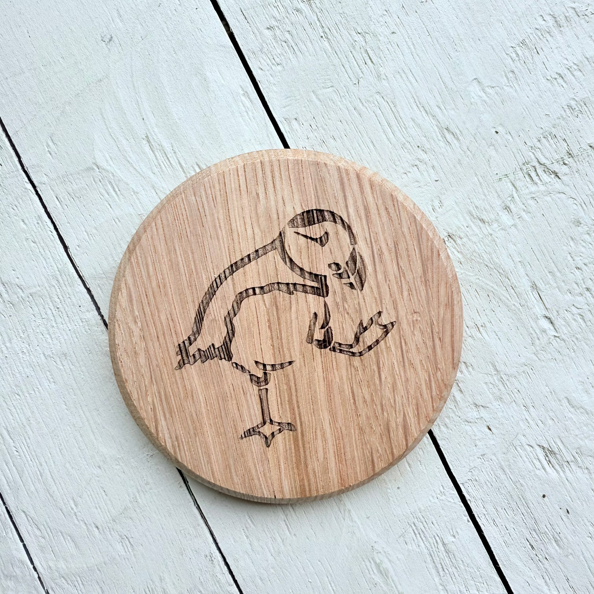 Barrel Oak Wooden circle coaster with a engraved puffin design on a light wooden surface